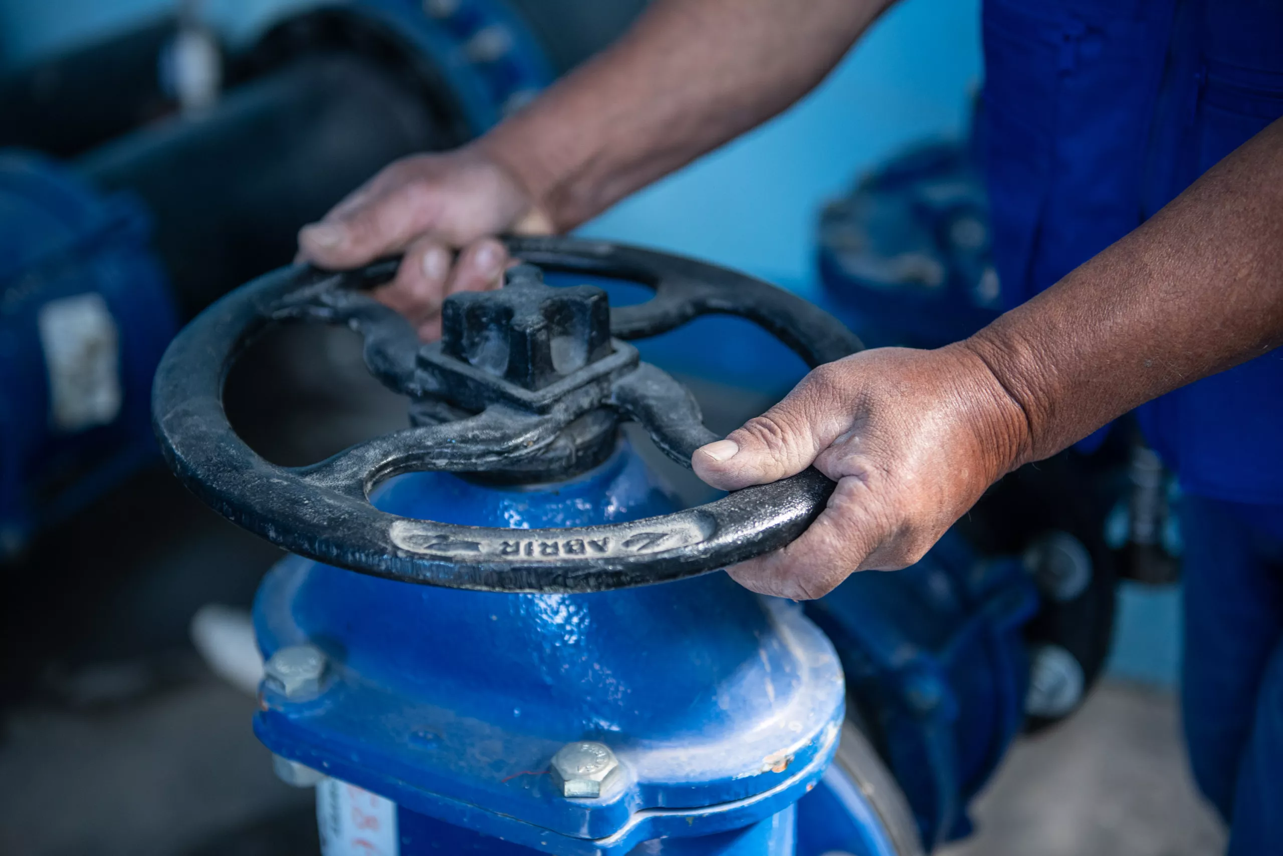 Worker's hands turning a large valve on industrial equipment.
